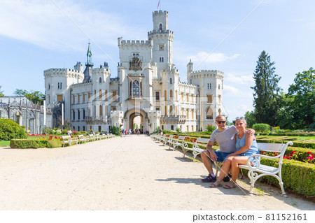 A couple of tourists are sitting on a bench in front of the beautiful castle Hluboka nad Vltavou - Czech Republic. A couple of tourists are sitting on a bench in front of the beautiful castle Hluboka nad Vltavou - Czech Republic. 81152161