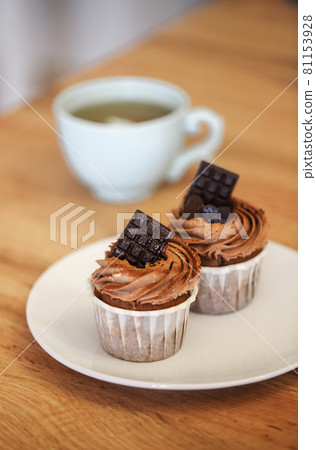 Two freshly baked muffins on plate decorated with cocoa cream and pieces of chocolate Two freshly baked muffins on plate decorated with cocoa cream and pieces of chocolate 81153928