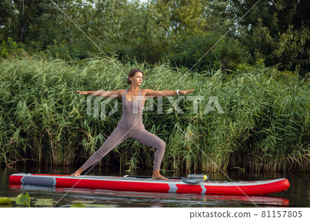 One young Caucasian beautiful slim girl doing yoga, pilates on paddle board, SUP alone in summer morning. Active life, sport, leisure activity concept One young Caucasian beautiful slim girl doing yoga, pilates on paddle board, SUP alone in summer morning. Active life, sport, leisure activity concept 81157805