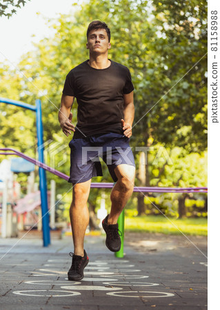 One young handsome caucasian man in sportswear training, exercising on sports ground outdoors on bright summer day. 81158988