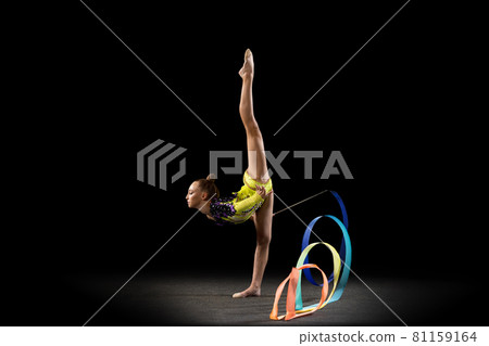 Slim sportive girl, rhythmic gymnastics artist in bright stage costume isolated on dark studio background in ray of light. Concept of sport, action, aspiration, active lifestyle 81159164