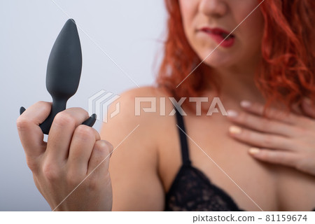 Excited red-haired woman in underwear holds a black anal plug in her hands on a white background Excited red-haired woman in underwear holds a black anal plug in her hands on a white background 81159674