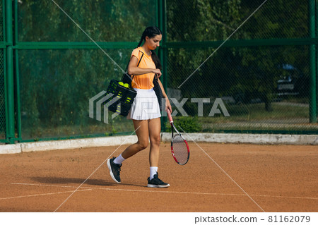 One young sportswoman, professional tennis player with racket practicing on clay tennis court in summer day. One young sportswoman, professional tennis player with racket practicing on clay tennis court in summer day. 81162079