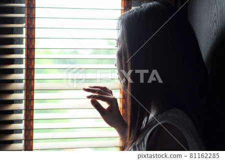 Rear view portrait of lonely woman looks out the window through the wooden curtain Rear view portrait of lonely woman looks out the window through the wooden curtain 81162285