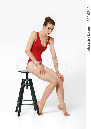 Model tests in red body swimming suit posing in studio with a chair Model tests in red body swimming suit posing in studio with a chair 81162464