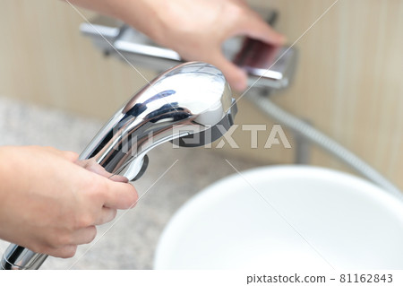 Female hand twisting the shower faucet 81162843