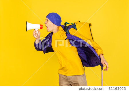 Comic portrait of young man, delivery guy in uniform isolated on yellow studio background. Concept of humor, safety, service. Complementary colors Comic portrait of young man, delivery guy in uniform isolated on yellow studio background. Concept of humor, safety, service. Complementary colors 81163023