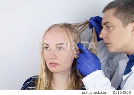 A trichologist examines a girl with oily hair. Problematic scalp and increased secretion of the sebaceous glands. Hair care. Oily hair care and treatment concept. Doctor prescribes treatment. 81164809