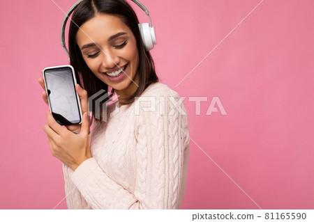 Pretty young brunette woman wearing pink casual sweater isolated over pink background wall wearing 81165590