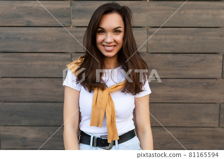 Portrait of young beautiful positive happy brunette woman standing against brown wall in the street Portrait of young beautiful positive happy brunette woman standing against brown wall in the street 81165594