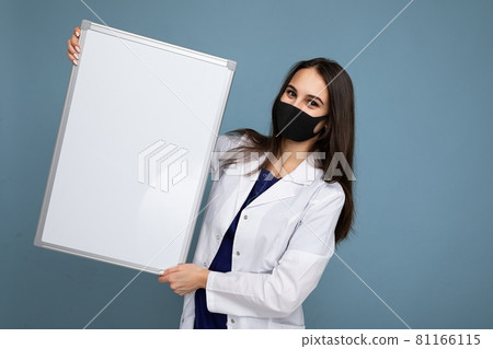 Woman doctor wearing a white medical coat and a mask holding blank board with copy space for text 81166115