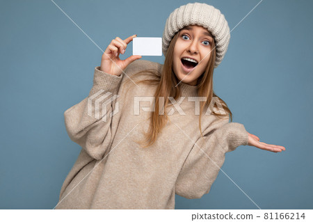 Beautiful shocked positive smiling young dark blonde woman wearing beige sweater and knitted beige Beautiful shocked positive smiling young dark blonde woman wearing beige sweater and knitted beige 81166214