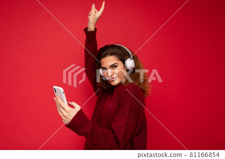 Shot of beautiful young brunette curly woman wearing dark red sweater isolated over red background 81166854