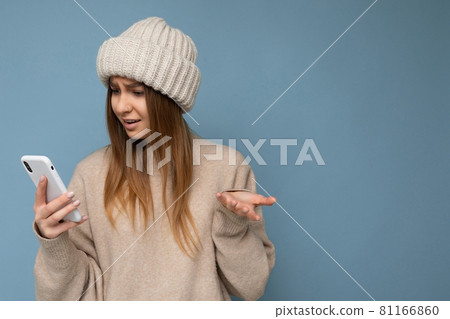 Photo of beautiful young shocked blonde woman wearing stylish beige warm sweater and knitted winter 81166860