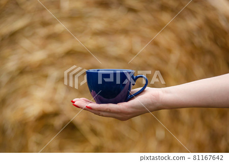 Female hand holds a porcelain cup of coffee on a natural background. Selective focus on the cup. 81167642