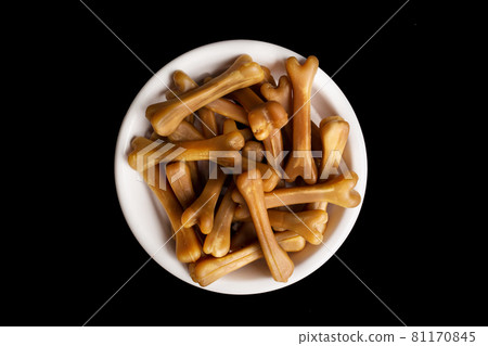 Close-up of brown dog food bones in a white dog bowl on a black studio background. Close-up of brown dog food bones in a white dog bowl on a black studio background. 81170845
