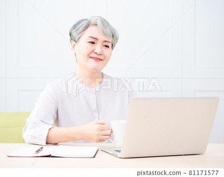 Asian mature woman using wireless laptop to browse internet and drink coffee. 81171577