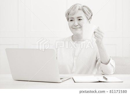 Asian mature woman using wireless laptop to browse internet and drink coffee. 81171580