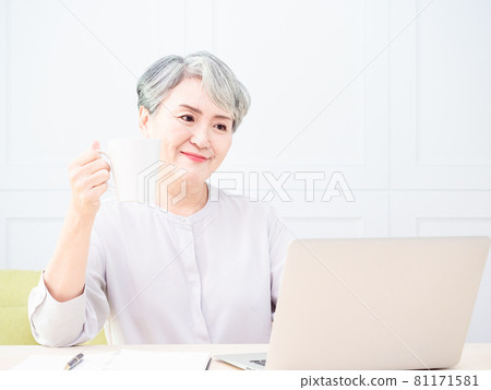 Asian mature woman using wireless laptop to browse internet and drink coffee. 81171581