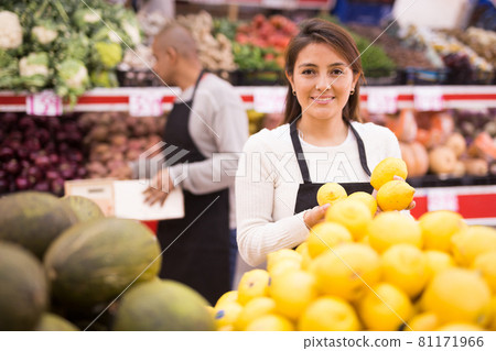 Latin supermarket woman employee in black apron and male assistant in background Latin supermarket woman employee in black apron and male assistant in background 81171966