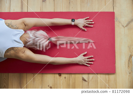 Pink haired lady with smartwatch in white top sits in child pose on floor Pink haired lady with smartwatch in white top sits in child pose on floor 81172098