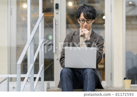 A young man sitting on the steps and operating a laptop A young man sitting on the steps and operating a laptop 81172593