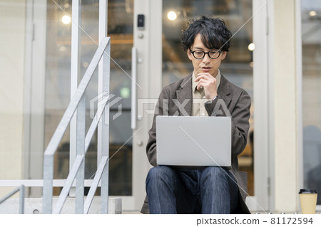 A young man sitting on the steps and operating a laptop A young man sitting on the steps and operating a laptop 81172594