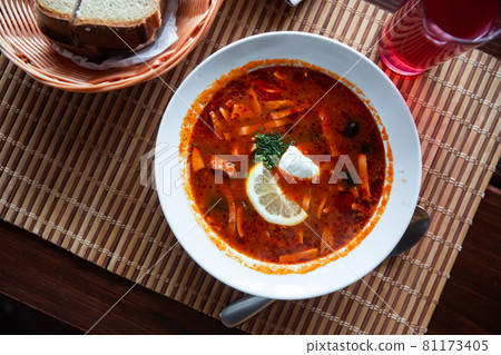 Delicious meat soup solyanka on broth served with sour cream and herbs Delicious meat soup solyanka on broth served with sour cream and herbs 81173405