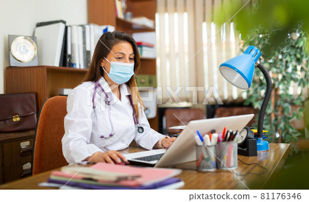 Hispanic woman doctor in face mask sitting in office Hispanic woman doctor in face mask sitting in office 81176346