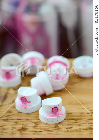 The soiled pink nozzles from the paint sprayer lies on a wooden plank on a background of a many dirty spray cans 81179156