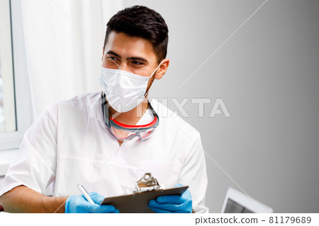 Mixed race male doctor sitting at his working table in hospital Mixed race male doctor sitting at his working table in hospital 81179689