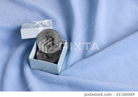 The silver bitcoin lies in a small blue gift box with a small bow on a blanket made of soft and fluffy light blue fleece fabric with a large number of relief folds The silver bitcoin lies in a small blue gift box with a small bow on a blanket made of soft and fluffy light blue fleece fabric with a large number of relief folds 81180084