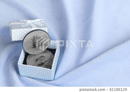 The silver bitcoin lies in a small blue gift box with a small bow on a blanket made of soft and fluffy light blue fleece fabric with a large number of relief folds The silver bitcoin lies in a small blue gift box with a small bow on a blanket made of soft and fluffy light blue fleece fabric with a large number of relief folds 81180129