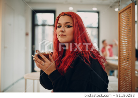 European plus size woman. Young red pink haired body positive girl sitting in cafe with coffee drink. 81180288