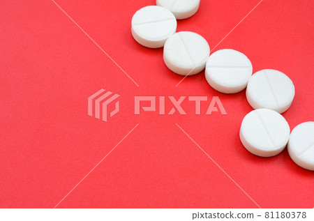 A few white tablets lie on a bright red background surface. Background image on medical and pharmaceutical topics A few white tablets lie on a bright red background surface. Background image on medical and pharmaceutical topics 81180378