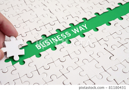 The human hand paves the way to the surface of the jigsaw puzzle, forming a green space with inscription. Business way The human hand paves the way to the surface of the jigsaw puzzle, forming a green space with inscription. Business way 81180431