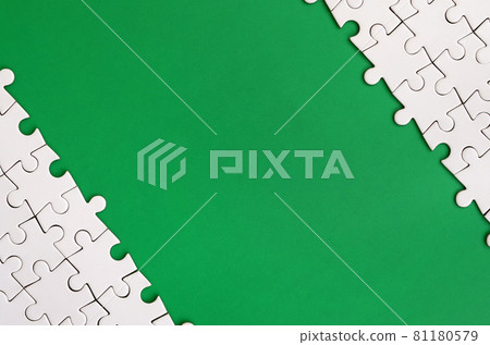 Fragment of a folded white jigsaw puzzle on the background of a green plastic surface. Texture photo with copy space for text Fragment of a folded white jigsaw puzzle on the background of a green plastic surface. Texture photo with copy space for text 81180579
