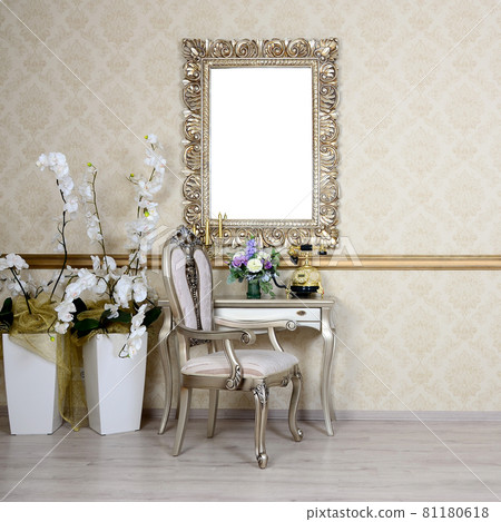 A fragment of a retro interior with a chair and table, on which is a telephone and a vase of flowers. Above the table hangs an empty picture frame for your photo A fragment of a retro interior with a chair and table, on which is a telephone and a vase of flowers. Above the table hangs an empty picture frame for your photo 81180618