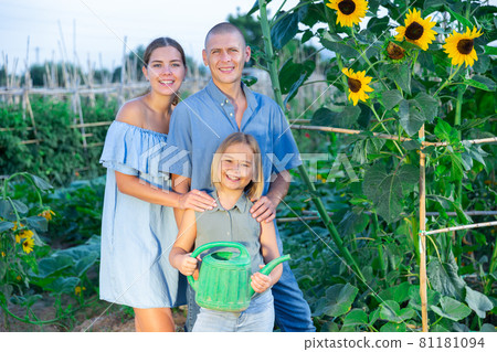 Portrait of daughter and parents with watering cans in summer garden Portrait of daughter and parents with watering cans in summer garden 81181094