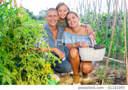 Portrait of daughter and parents with watering cans in summer garden Portrait of daughter and parents with watering cans in summer garden 81181095