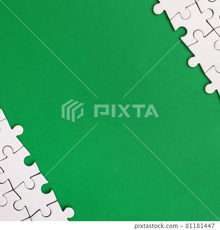 Fragment of a folded white jigsaw puzzle on the background of a green plastic surface. Texture photo with copy space for text Fragment of a folded white jigsaw puzzle on the background of a green plastic surface. Texture photo with copy space for text 81181447