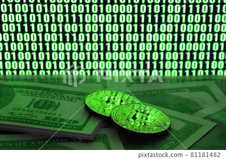 Two bitcoins lies on a pile of dollar bills on the background of a monitor depicting a binary code of bright green zeros and one units on a black background. Low key lighting 81181482
