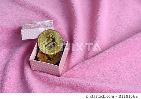 The golden bitcoin lies in a small pink gift box with a small bow on a blanket made of soft and fluffy light pink fleece fabric with a large number of relief folds The golden bitcoin lies in a small pink gift box with a small bow on a blanket made of soft and fluffy light pink fleece fabric with a large number of relief folds 81181569