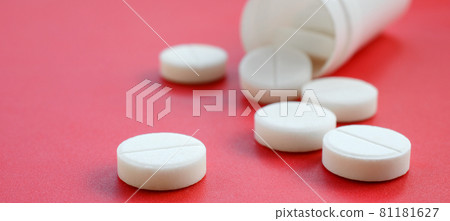 Several white tablets fall out of the plastic jar on the red surface. Background image on medical and pharmaceutical topics 81181627