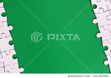 Fragment of a folded white jigsaw puzzle on the background of a green plastic surface. Texture photo with copy space for text Fragment of a folded white jigsaw puzzle on the background of a green plastic surface. Texture photo with copy space for text 81182460