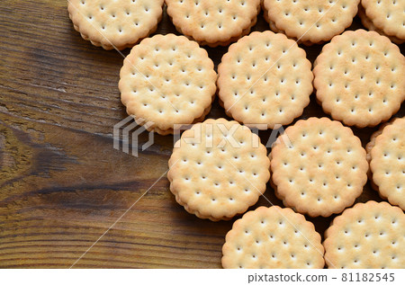 A round sandwich cookie with coconut filling lies in large quantities on a brown wooden surface. Photo of edible treats on a wooden background with copy space 81182545