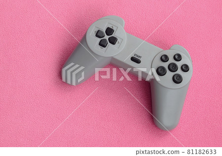 Playing games concept. Single pad joystick lies on the blanket of furry pink fleece fabric. Controller for video games on a background texture of light pink soft plush fleece material 81182633