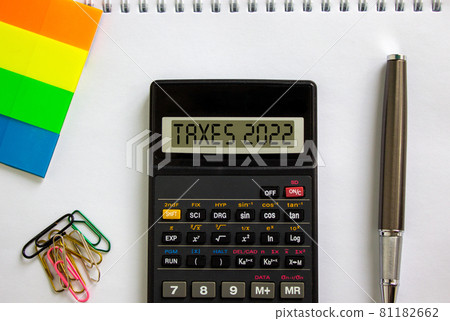 Business concept of taxes planning 2022. Calculator with words 'Taxes 2022', white note, colored paper, paper clips, pen. Beautiful white background, copy space. Business, 2022 taxes concept. 81182662