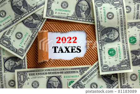 2022 taxes new year symbol. Words '2022 taxes' appearing behind torn brown paper. Beautiful background from dollar bills. Business, 2022 taxes new year concept, copy space. 81183089