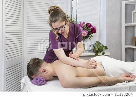 Woman massage therapist gives massage to young man. Wellness procedure. Professional massage the back at spa salon. Woman massage therapist gives massage to young man. Wellness procedure. Professional massage the back at spa salon. 81183264